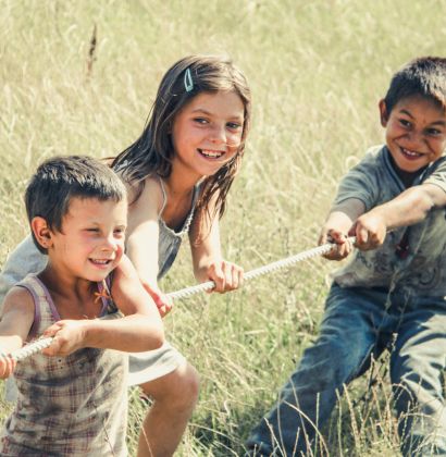 3 Kinder beim Tau ziehen auf einer Wiese